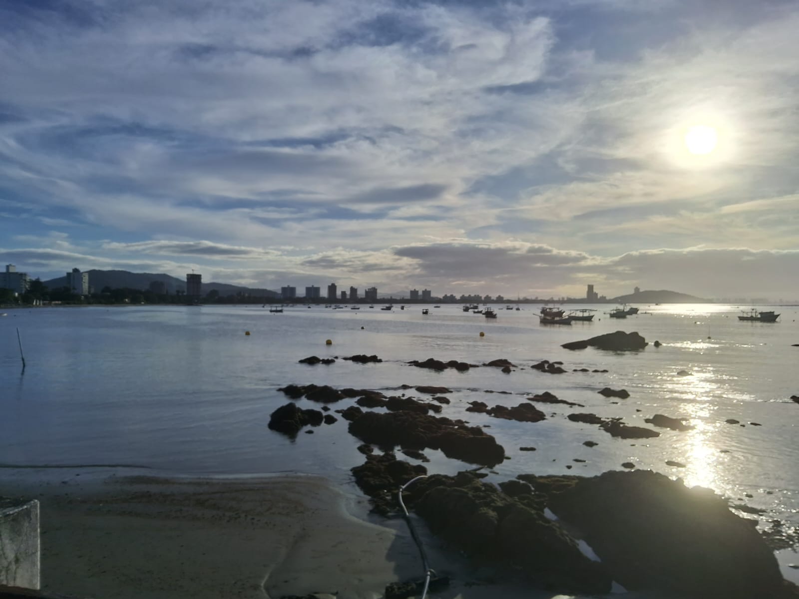 paisagem à beira mar na localidade Itapocorói em Penha (SC), mostrando a silhueta da cidade ao fundo em um fim de tarde ensolarado